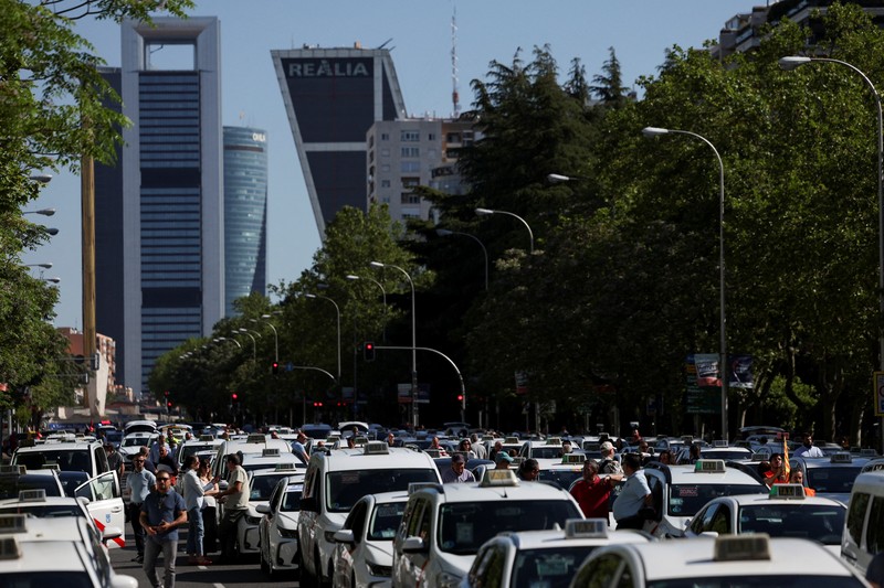 People cross a street as taxi drivers take part in a protest march against ride-hailing vehicles, in Madrid, Spain, May 28, 2025. REUTERS/Violeta Santos Moura
