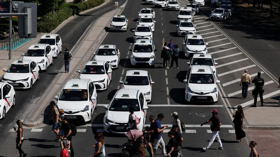 People cross a street as taxi drivers take part in a protest march against ride-hailing vehicles, in Madrid, Spain, May 28, 2025. REUTERS/Violeta Santos Moura