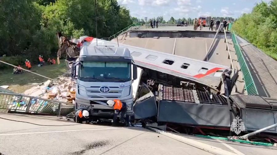 Petugas layanan darurat berada pada lokasi gerbong kereta yang rusak setelah jembatan jalan runtuh ke rel kereta api di wilayah Bryansk, Rusia, Minggu (1/6/2025). (Russian Emergencies Ministry/Handout via REUTERS)
