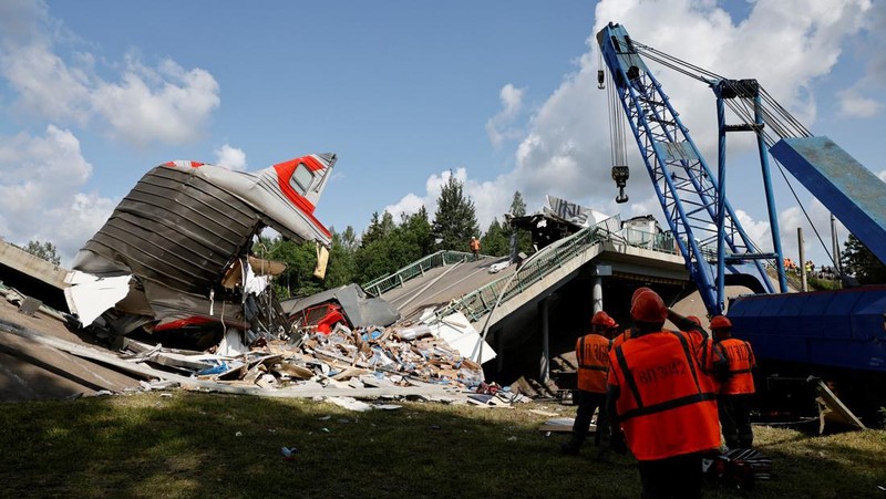 Petugas layanan darurat berada pada lokasi gerbong kereta yang rusak setelah jembatan jalan runtuh ke rel kereta api di wilayah Bryansk, Rusia, Minggu (1/6/2025). (Russian Emergencies Ministry/Handout via REUTERS)