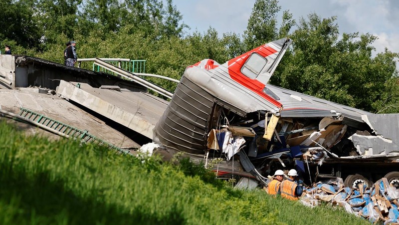Petugas layanan darurat berada pada lokasi gerbong kereta yang rusak setelah jembatan jalan runtuh ke rel kereta api di wilayah Bryansk, Rusia, Minggu (1/6/2025). (Russian Emergencies Ministry/Handout via REUTERS)