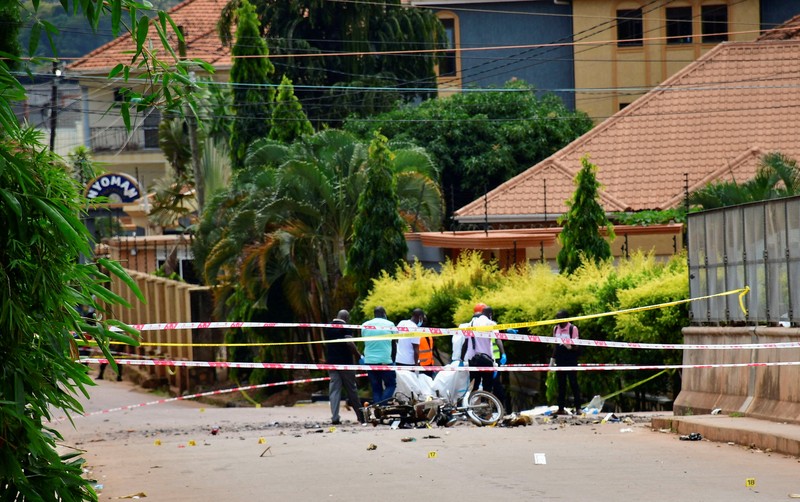 Orang-orang menyaksikan para ahli forensik mengamankan lokasi ledakan bom di dekat Kuil Martir Munyonyo, sebuah kuil Katolik Roma saat warga Uganda berkumpul untuk merayakan Hari Martir, yang memperingati umat Kristen yang terbunuh karena iman mereka pada abad ke-19, di pinggiran kota Munyonyo, Kampala, Uganda, 3 Juni 2025. (REUTERS/Abubaker Lubowa)