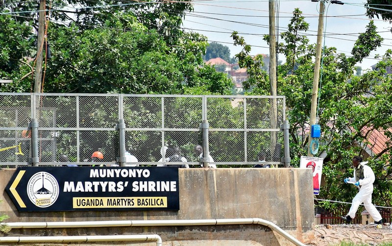 Orang-orang menyaksikan para ahli forensik mengamankan lokasi ledakan bom di dekat Kuil Martir Munyonyo, sebuah kuil Katolik Roma saat warga Uganda berkumpul untuk merayakan Hari Martir, yang memperingati umat Kristen yang terbunuh karena iman mereka pada abad ke-19, di pinggiran kota Munyonyo, Kampala, Uganda, 3 Juni 2025. (REUTERS/Abubaker Lubowa)