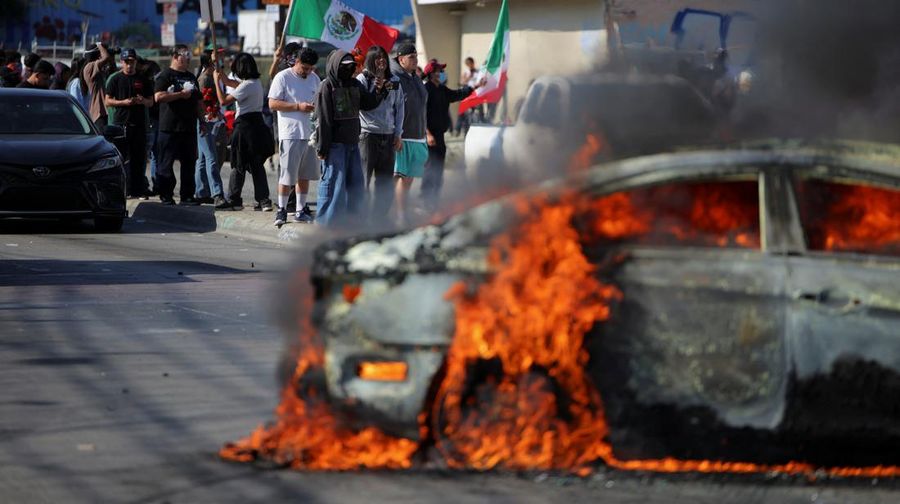 A Mexican flag waves as a car burns in flames following multiple detentions by Immigration and Customs Enforcement (ICE), in the Los Angeles County city of Paramount, California, U.S., June 7, 2025.   REUTERS/Daniel Cole