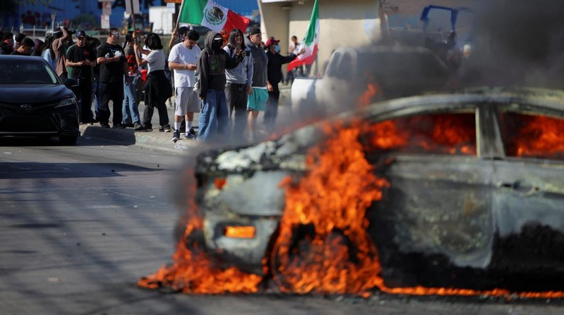 A Mexican flag waves as a car burns in flames following multiple detentions by Immigration and Customs Enforcement (ICE), in the Los Angeles County city of Paramount, California, U.S., June 7, 2025.   REUTERS/Daniel Cole