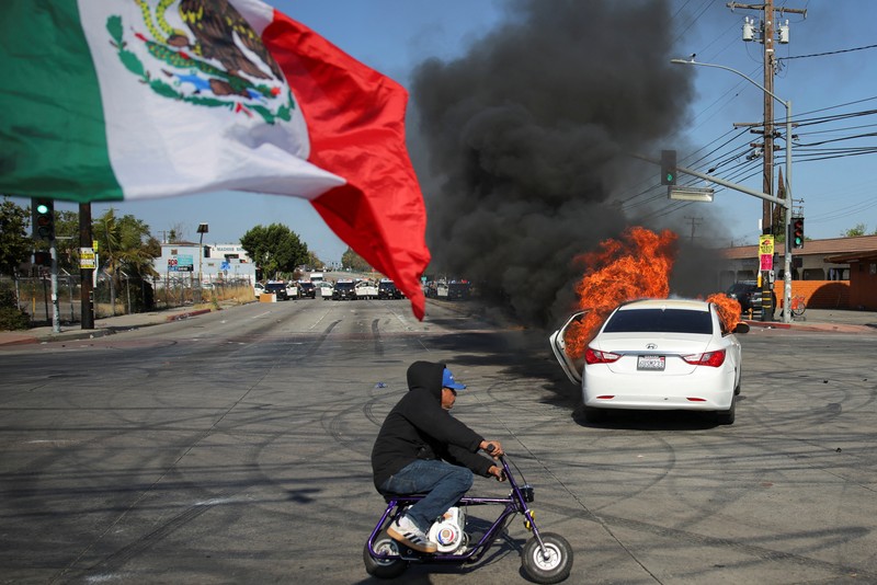 A Mexican flag waves as a car burns in flames following multiple detentions by Immigration and Customs Enforcement (ICE), in the Los Angeles County city of Paramount, California, U.S., June 7, 2025.   REUTERS/Daniel Cole