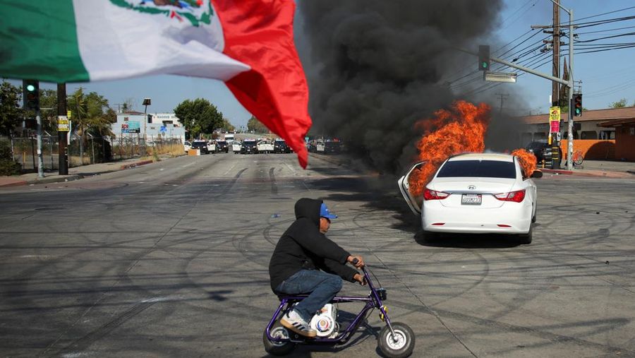 A Mexican flag waves as a car burns in flames following multiple detentions by Immigration and Customs Enforcement (ICE), in the Los Angeles County city of Paramount, California, U.S., June 7, 2025.   REUTERS/Daniel Cole