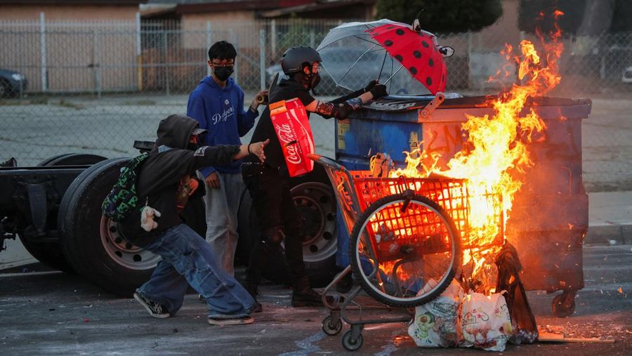 Protesters stand next to a burning shopping cart during a standoff between police and protesters following multiple detentions by Immigration and Customs Enforcement (ICE), in the Los Angeles County city of Paramount, California, U.S., June 7, 2025. REUTERS/Daniel Cole