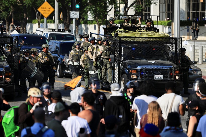 Para demonstran berkumpul di depan pasukan Garda Nasional California dan petugas penegak hukum, saat protes terhadap pemeriksaan imigrasi berlanjut, di Los Angeles, California, AS, 9 Juni 2025. Para demonstran berkumpul di depan pasukan Garda Nasional California dan petugas penegak hukum, saat protes terhadap pemeriksaan imigrasi berlanjut, di Los Angeles, California, AS, 9 Juni 2025. (REUTERS/Daniel Cole)