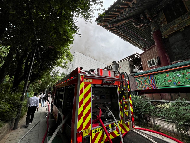 Orang-orang berjalan melewati mobil pemadam kebakaran saat kebakaran terjadi di gedung Museum Buddha Pusat di sebelah Kuil Jogye di Seoul, Korea Selatan, 10 Juni 2025. (REUTERS/Josh Smith)