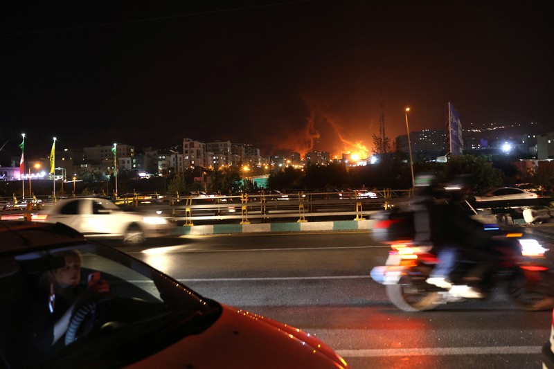 Orang-orang menyaksikan dari jembatan saat api dari serangan Israel membubung dari depot minyak Sharan, menyusul serangan Israel terhadap Iran, di Teheran, Iran, 15 Juni 2025. Orang-orang menyaksikan dari jembatan saat api dari serangan Israel membubung dari depot minyak Sharan, menyusul serangan Israel terhadap Iran, di Teheran, Iran, 15 Juni 2025. (Majid Asgaripour/WANA (West Asia News Agency) via REUTERS)