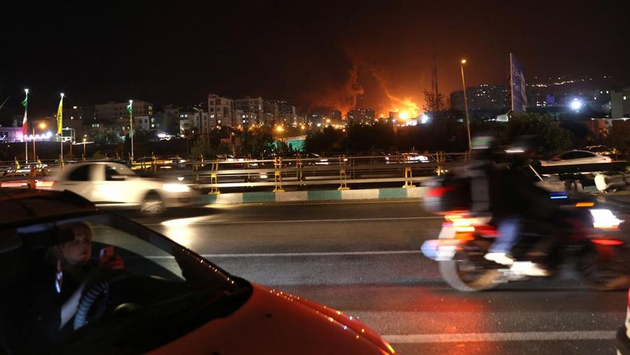 Orang-orang menyaksikan dari jembatan saat api dari serangan Israel membubung dari depot minyak Sharan, menyusul serangan Israel terhadap Iran, di Teheran, Iran, 15 Juni 2025. (Majid Asgaripour/WANA (West Asia News Agency) via REUTERS)