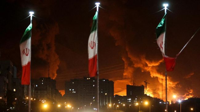 Bendera Iran berkibar saat api dan asap dari serangan Israel terhadap depot minyak Sharan membubung, menyusul serangan Israel terhadap Iran, di Teheran, Iran, 15 Juni 2025. (Majid Asgaripour/WANA (West Asia News Agency) via REUTERS)