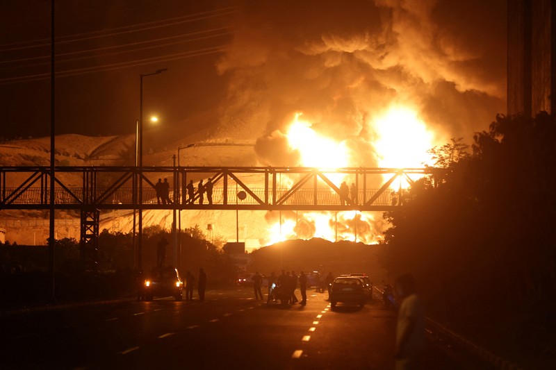 Orang-orang menyaksikan dari jembatan saat api dari serangan Israel membubung dari depot minyak Sharan, menyusul serangan Israel terhadap Iran, di Teheran, Iran, 15 Juni 2025. Orang-orang menyaksikan dari jembatan saat api dari serangan Israel membubung dari depot minyak Sharan, menyusul serangan Israel terhadap Iran, di Teheran, Iran, 15 Juni 2025. (Majid Asgaripour/WANA (West Asia News Agency) via REUTERS)