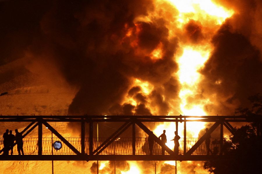 Orang-orang menyaksikan dari jembatan saat api dari serangan Israel membubung dari depot minyak Sharan, menyusul serangan Israel terhadap Iran, di Teheran, Iran, 15 Juni 2025.