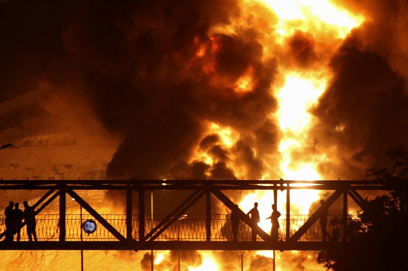 Orang-orang menyaksikan dari jembatan saat api dari serangan Israel membubung dari depot minyak Sharan, menyusul serangan Israel terhadap Iran, di Teheran, Iran, 15 Juni 2025. (Majid Asgaripour/WANA (West Asia News Agency) via REUTERS)