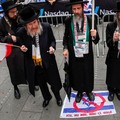 Seorang anggota Neturei Karta, kelompok Yahudi pinggiran yang menentang negara Israel, berdiri di atas tanda dengan bendera Israel dengan simbol larangan di atasnya saat ia dan yang lainnya mengambil bagian dalam protes untuk mendukung Iran dan Pales