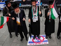 Seorang anggota Neturei Karta, kelompok Yahudi pinggiran yang menentang negara Israel, berdiri di atas tanda dengan bendera Israel dengan simbol larangan di atasnya saat ia dan yang lainnya mengambil bagian dalam protes untuk mendukung Iran dan Pales