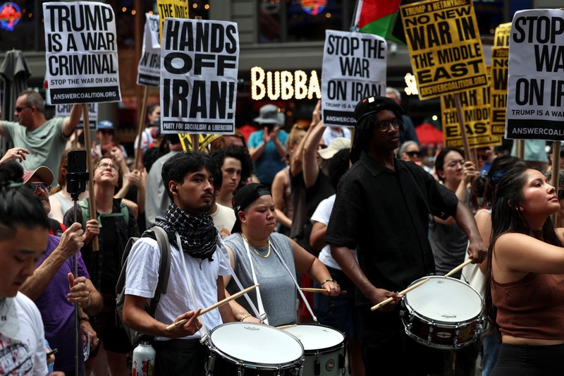 Marinir AS berjaga saat seorang demonstran memegang plakat selama protes terhadap Amerika Serikat yang bergabung dengan Israel dalam serangan terhadap fasilitas nuklir Iran, di gedung federal di Los Angeles, California, AS, 22 Juni 2025. (REUTERS/David Swanson)