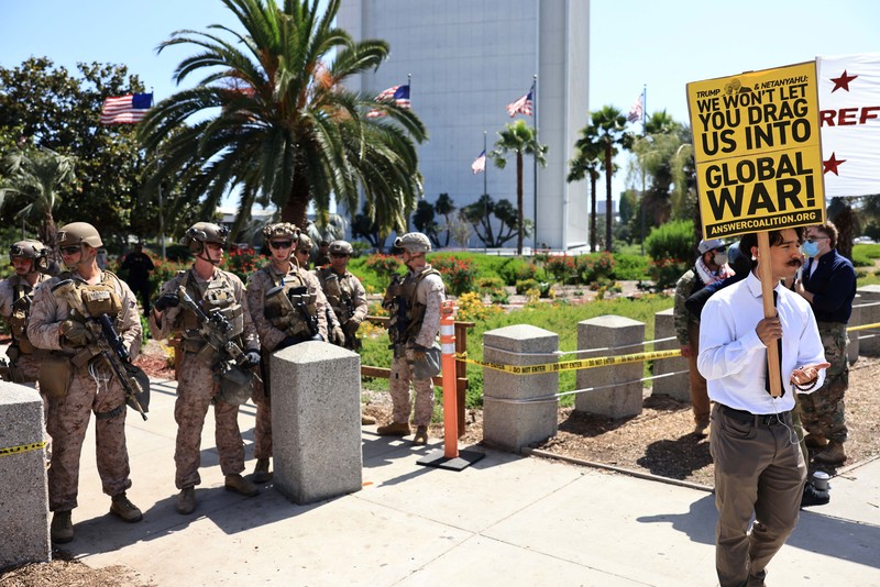 Marinir AS berjaga saat seorang demonstran memegang plakat selama protes terhadap Amerika Serikat yang bergabung dengan Israel dalam serangan terhadap fasilitas nuklir Iran, di gedung federal di Los Angeles, California, AS, 22 Juni 2025. (REUTERS/David Swanson)