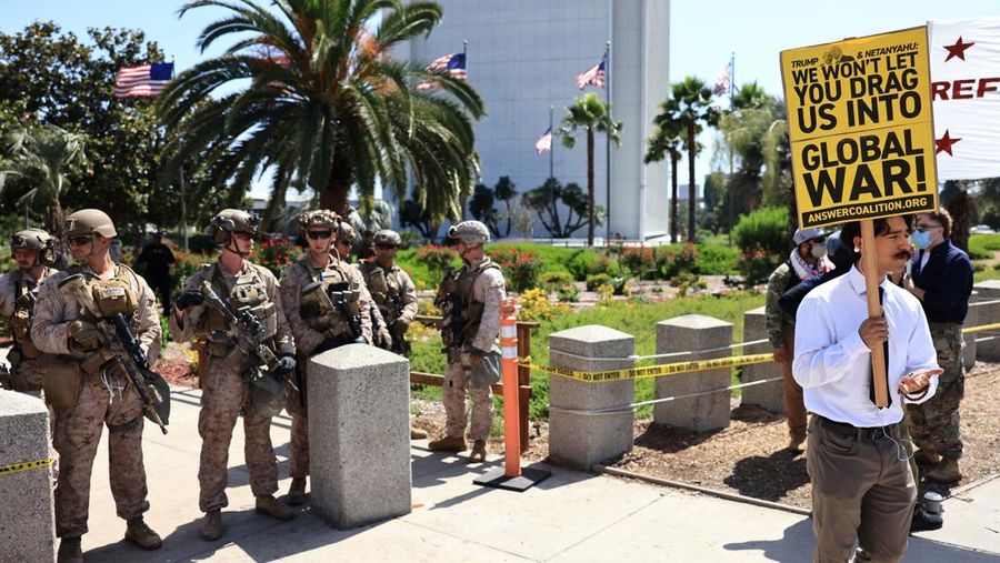 Marinir AS berjaga saat seorang demonstran memegang plakat selama protes terhadap Amerika Serikat yang bergabung dengan Israel dalam serangan terhadap fasilitas nuklir Iran, di gedung federal di Los Angeles, California, AS, 22 Juni 2025. (REUTERS/David Swanson)