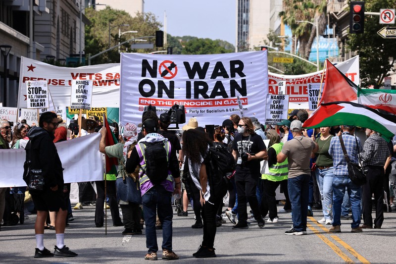 Marinir AS berjaga saat seorang demonstran memegang plakat selama protes terhadap Amerika Serikat yang bergabung dengan Israel dalam serangan terhadap fasilitas nuklir Iran, di gedung federal di Los Angeles, California, AS, 22 Juni 2025. (REUTERS/David Swanson)