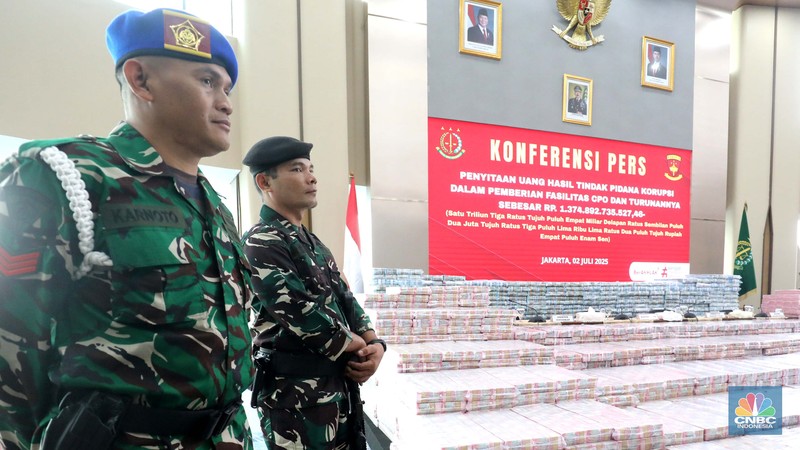 Petugas berjaga di samping tumpukan uang yang menjadi barang bukti uang sitaan saat konferensi pers kasus korupsi ekspor crude palm oil (CPO) di Gedung Bundar Jampidus Kejaksaaan Agung (Kejagung), Jakarta, Rabu (2/7/2025). (CNBC Indonesia/Muhammad Sabki)
