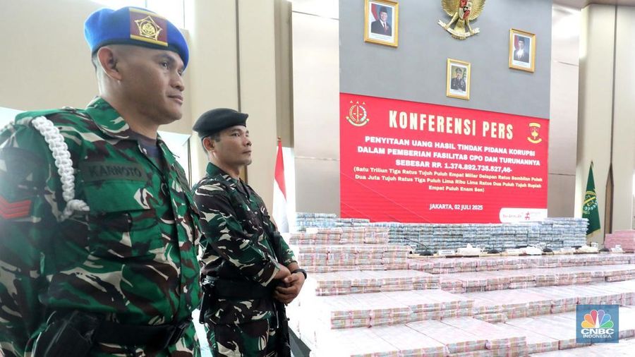 Petugas berjaga di samping tumpukan uang yang menjadi barang bukti uang sitaan saat konferensi pers kasus korupsi ekspor crude palm oil (CPO) di Gedung Bundar Jampidus Kejaksaaan Agung (Kejagung), Jakarta, Rabu (2/7/2025). (CNBC Indonesia/Muhammad Sabki)