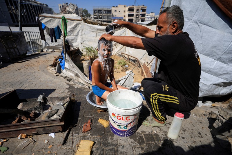 Seorang pria Palestina, yang mengungsi akibat serangan Israel, memandikan putranya di dalam tempat penampungan mereka di tengah teriknya musim panas, di Kota Gaza, 3 Juli 2025. Seorang pria Palestina, yang mengungsi akibat serangan Israel, memandikan putranya di dalam tempat penampungan mereka di tengah teriknya musim panas, di Kota Gaza, 3 Juli 2025. (REUTERS/Dawoud Abu Alkas)