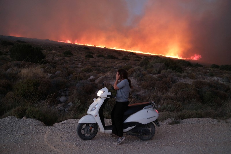 Seorang wanita bereaksi saat mencoba meninggalkan daerah tersebut dengan skuternya, selama kebakaran hutan di dekat Alacati, di provinsi Izmir, Turki, 3 Juli 2025. (REUTERS/Murat Kocabas)