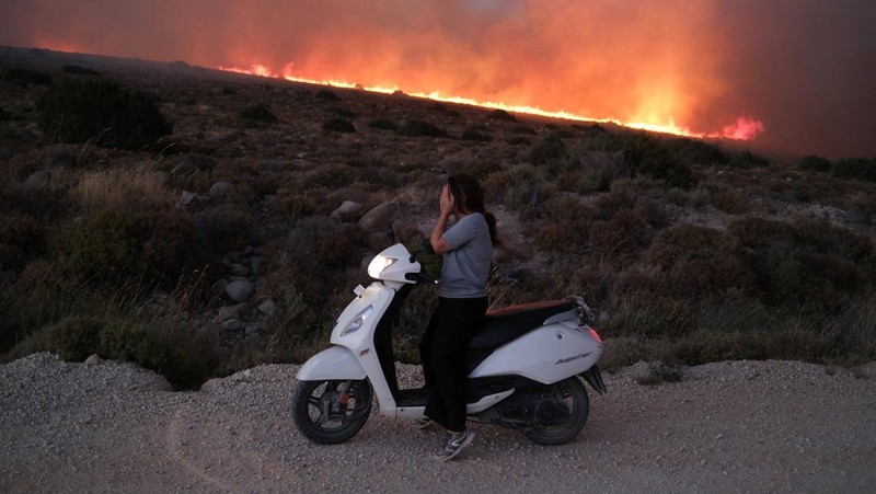 Seorang wanita bereaksi saat mencoba meninggalkan daerah tersebut dengan skuternya, selama kebakaran hutan di dekat Alacati, di provinsi Izmir, Turki, 3 Juli 2025. (REUTERS/Murat Kocabas)