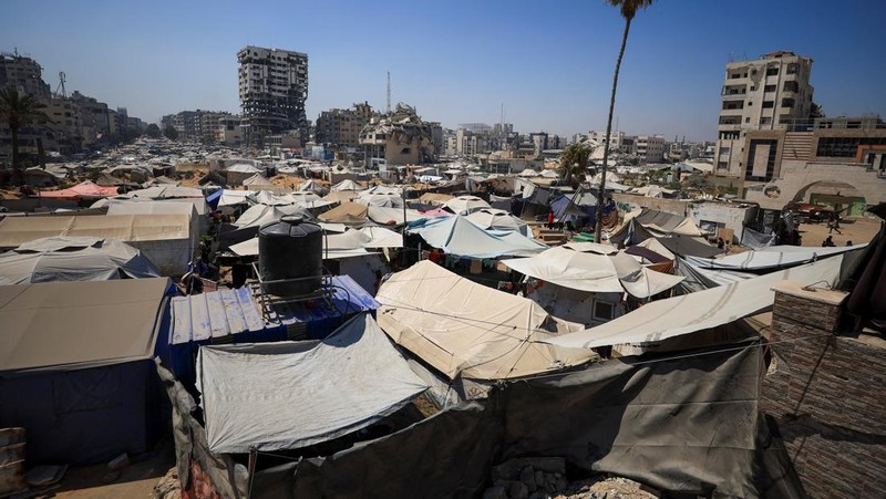 Seorang pria Palestina, yang mengungsi akibat serangan Israel, memandikan putranya di dalam tempat penampungan mereka di tengah teriknya musim panas, di Kota Gaza, 3 Juli 2025. (REUTERS/Dawoud Abu Alkas)