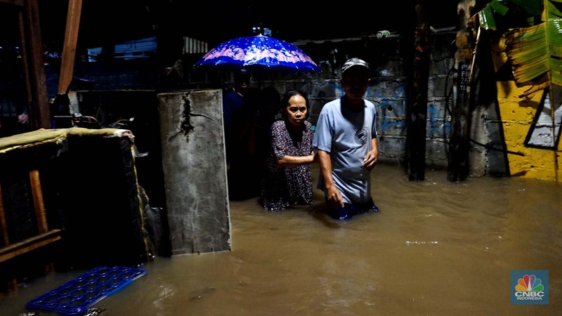Sejumlah warga melintas di tengah banjir di RW 06 Jatipadang, Jakarta Selatan, (6/7/2025). (CNBC Indonesia/Muhammad Sabki)