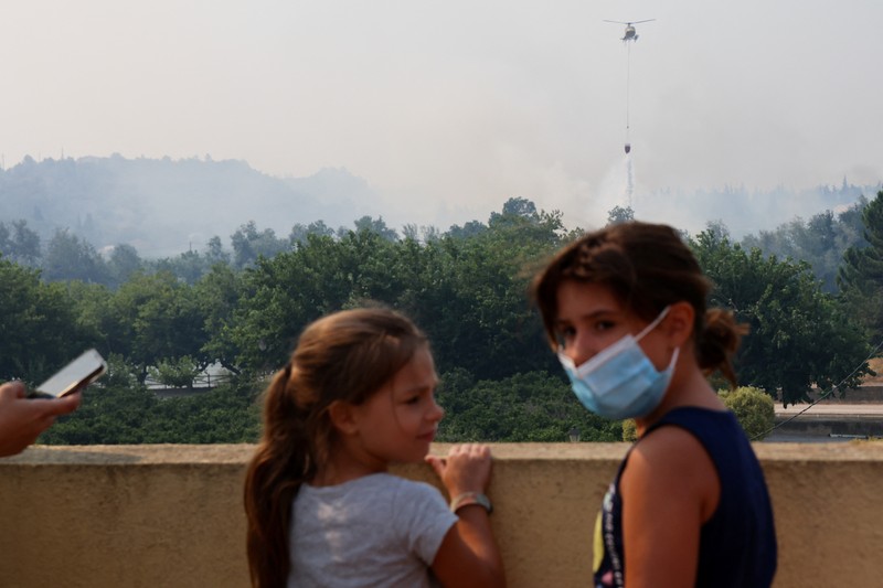 Anak-anak menyaksikan helikopter terbang untuk membantu memadamkan kebakaran hutan yang terjadi di Xerta, salah satu desa terkurung di provinsi Tarragona di Catalonia, Spanyol, 8 Juli 2025. Anak-anak menyaksikan helikopter terbang untuk membantu memadamkan kebakaran hutan yang terjadi di Xerta, salah satu desa terkurung di provinsi Tarragona di Catalonia, Spanyol, 8 Juli 2025. (REUTERS/Nacho Doce)
