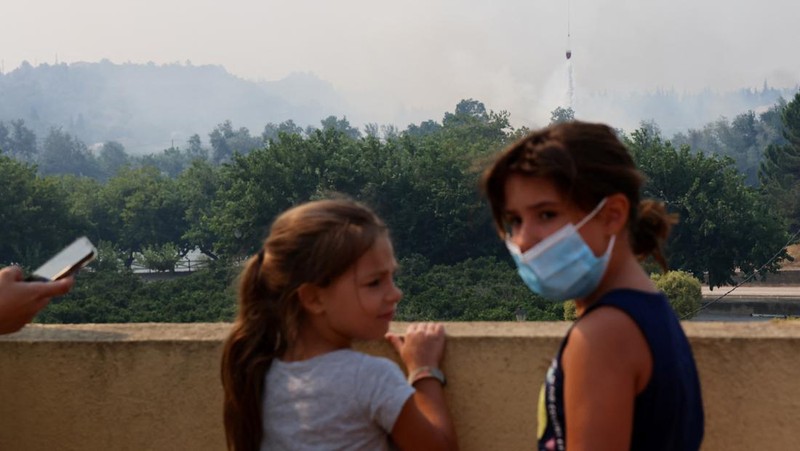 Anak-anak menyaksikan helikopter terbang untuk membantu memadamkan kebakaran hutan yang terjadi di Xerta, salah satu desa terkurung di provinsi Tarragona di Catalonia, Spanyol, 8 Juli 2025. (REUTERS/Nacho Doce)