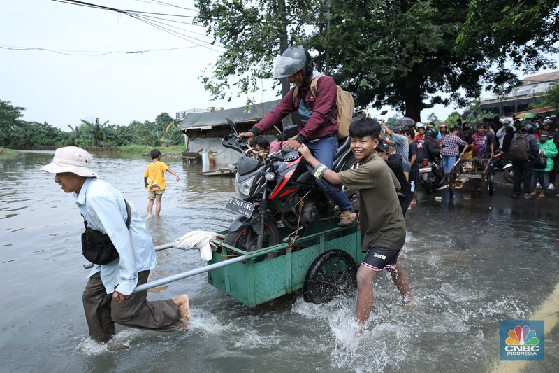 Sejumlah pengendara motor menggunakan jasa angkutan gerobak untuk melintasi genangan air yang membanjiri jalan Hasyim Ashari di Ciledug Indah, Tangerang, Banten, Selasa (8/7/2025). Sejumlah pengendara motor menggunakan jasa angkutan gerobak untuk melintasi genangan air yang membanjiri jalan Hasyim Ashari di Ciledug Indah, Tangerang, Banten, Selasa (8/7/2025). (CNBC Indonesia/Tri Susilo)