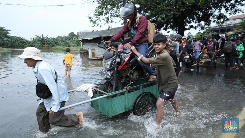 Sejumlah pengendara motor menggunakan jasa angkutan gerobak untuk melintasi genangan air yang membanjiri jalan Hasyim Ashari di Ciledug Indah, Tangerang, Banten, Selasa (8/7/2025). (CNBC Indonesia/Tri Susilo)