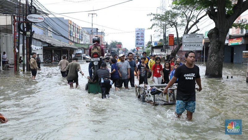 Sejumlah pengendara motor menggunakan jasa angkutan gerobak untuk melintasi genangan air yang membanjiri jalan Hasyim Ashari di Ciledug Indah, Tangerang, Banten, Selasa (8/7/2025). (CNBC Indonesia/Tri Susilo)