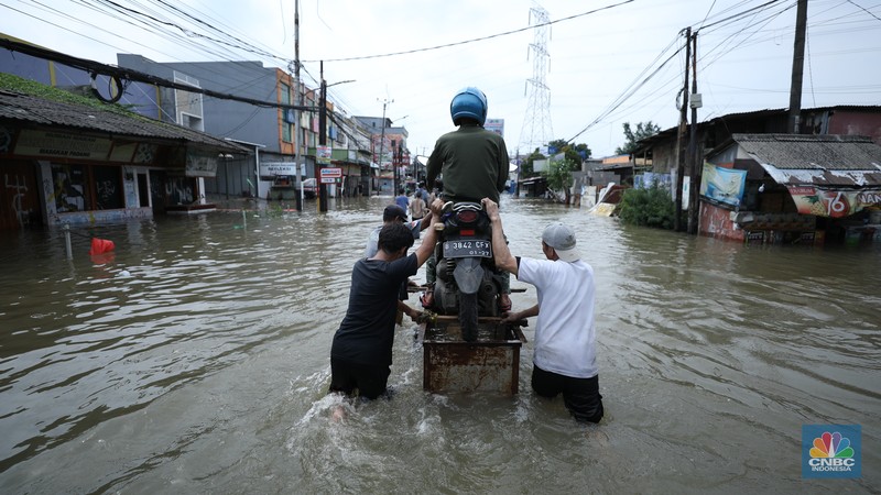 Sejumlah pengendara motor menggunakan jasa angkutan gerobak untuk melintasi genangan air yang membanjiri jalan Hasyim Ashari di Ciledug Indah, Tangerang, Banten, Selasa (8/7/2025). (CNBC Indonesia/Tri Susilo)