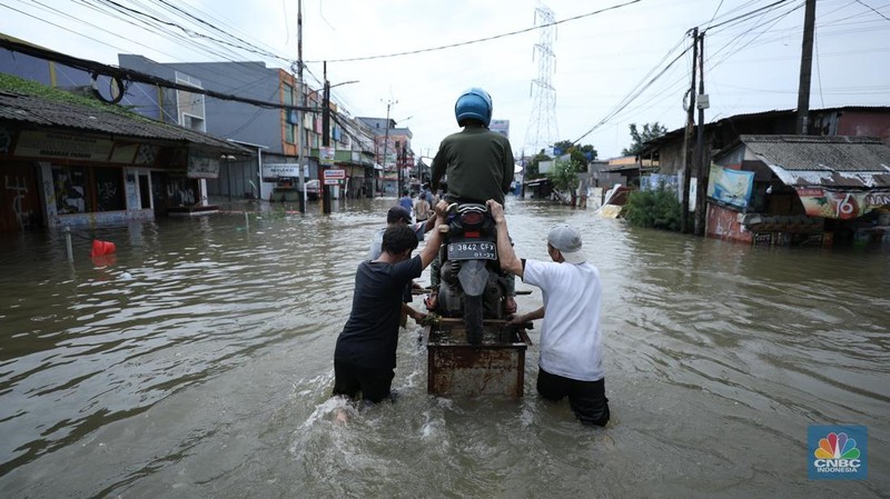 Sejumlah pengendara motor menggunakan jasa angkutan gerobak untuk melintasi genangan air yang membanjiri jalan Hasyim Ashari di Ciledug Indah, Tangerang, Banten, Selasa (8/7/2025). (CNBC Indonesia/Tri Susilo)
