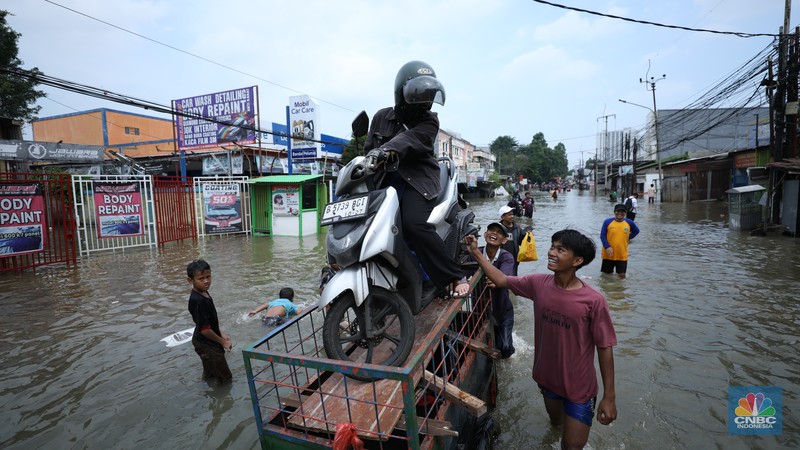 Sejumlah pengendara motor menggunakan jasa angkutan gerobak untuk melintasi genangan air yang membanjiri jalan Hasyim Ashari di Ciledug Indah, Tangerang, Banten, Selasa (8/7/2025). Sejumlah pengendara motor menggunakan jasa angkutan gerobak untuk melintasi genangan air yang membanjiri jalan Hasyim Ashari di Ciledug Indah, Tangerang, Banten, Selasa (8/7/2025). (CNBC Indonesia/Tri Susilo)