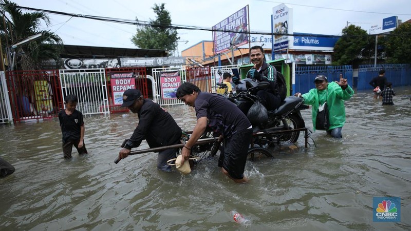Sejumlah pengendara motor menggunakan jasa angkutan gerobak untuk melintasi genangan air yang membanjiri jalan Hasyim Ashari di Ciledug Indah, Tangerang, Banten, Selasa (8/7/2025). (CNBC Indonesia/Tri Susilo)