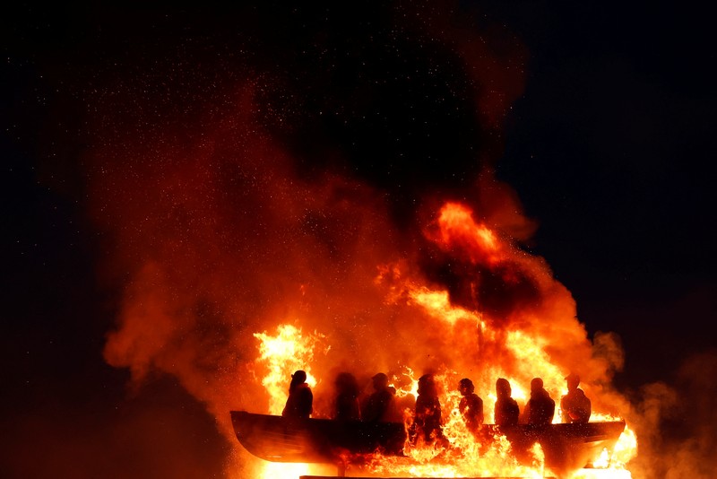 Tumpukan api unggun loyalis terlihat bersama model perahu berisi manekin yang digambarkan sebagai migran berjaket pelampung dengan tanda bertuliskan 