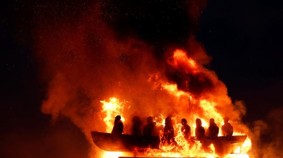 Tumpukan api unggun loyalis terlihat bersama model perahu berisi manekin yang digambarkan sebagai migran berjaket pelampung dengan tanda bertuliskan 