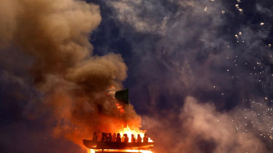 Tumpukan api unggun loyalis terlihat bersama model perahu berisi manekin yang digambarkan sebagai migran berjaket pelampung dengan tanda bertuliskan 