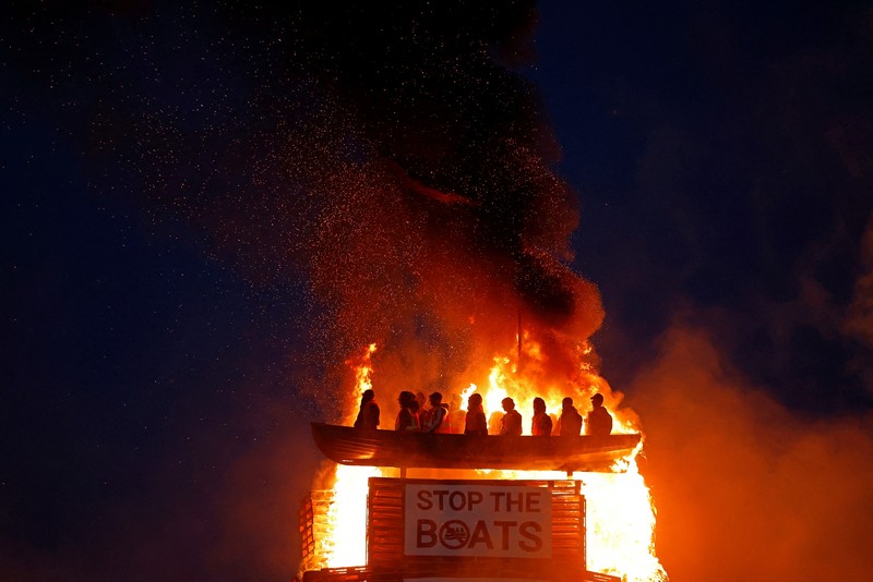 MIGRATION-NIRELAND/ A loyalist bonfire burns after being set alight, featuring a model effigy of a boat containing mannequins portrayed as migrants in lifejackets, with a sign reading