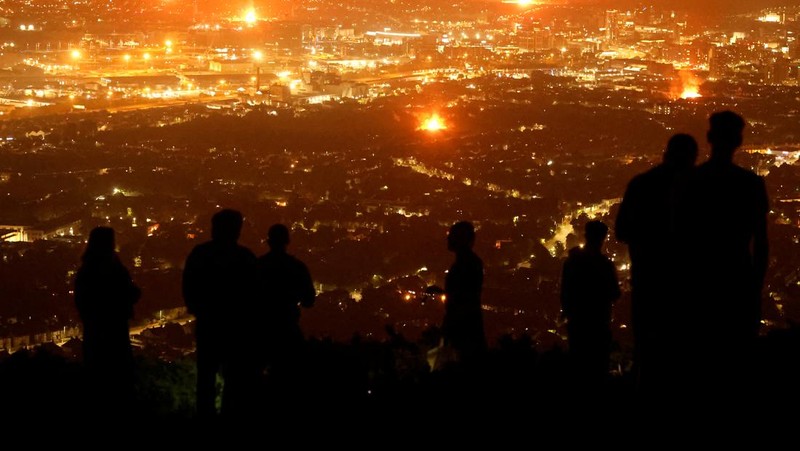 A loyalist bonfire burns after being set alight, featuring a model effigy of a boat containing mannequins portrayed as migrants in lifejackets, with a sign reading 
