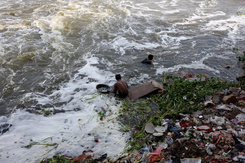 Ramu Gupta, seorang pria berusia 67 tahun yang pergi ke sungai untuk berburu koin dan barang berharga lainnya, mengeluarkan tas berisi plastik dari perairan sungai Yamuna di New Delhi, India, 26 Juni 2025. (REUTERS/Bhawika Chhabra)