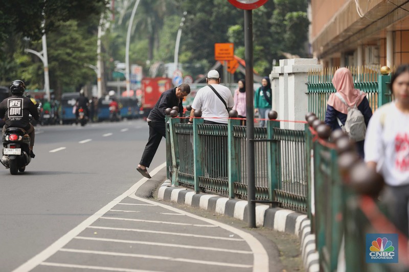 penumpang krl, commuterline, kai, Sejumlah warga calon penumpang commuterline melompati pagar pembatas antara jalan dan Stasiun Cikini di Jakarta, Jumat (18/7/2025). (CNBC Indonesia/Tri Susilo)