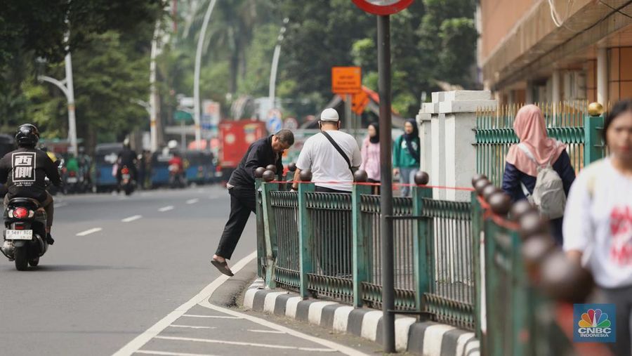 Sejumlah warga calon penumpang commuterline melompati pagar pembatas antara jalan dan Stasiun Cikini di Jakarta, Jumat (18/7/2025). (CNBC Indonesia/Tri Susilo)